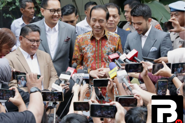 Mantan Presiden Joko Widodo mengenakan batik sedang berbicara di hadapan wartawan yang mengangkat ponsel dan mikrofon untuk merekam pernyataannya